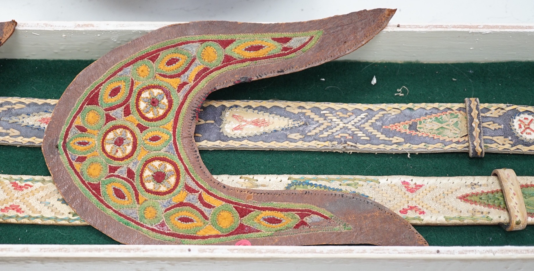 A two framed native American Indian ornately woven and embroidered leather belts and a pair of leather embroidered slipper fronts, longest belt 103cms